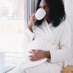 Femme enceinte buvant une boisson chaude près de la fenêtre